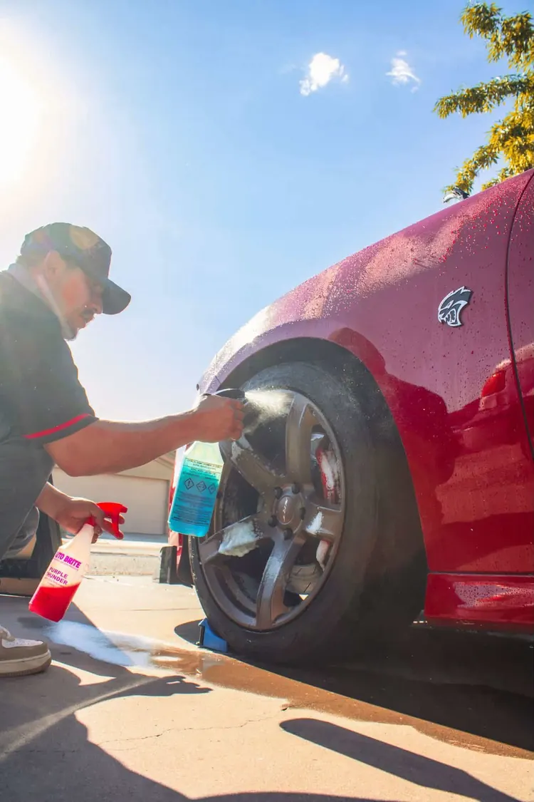Cleaning the wheel of a red Hellcat Charger in the sun
